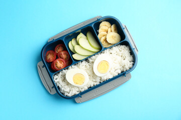 Lunch box with rice, fruits, tomatoes and egg halves on light blue background, top view