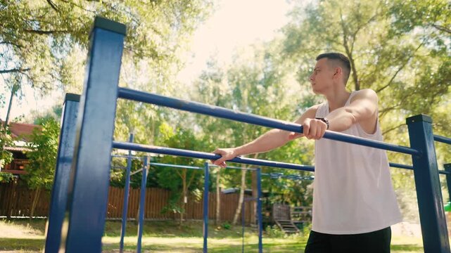 Handsome pumped up young male bodybuilder doing exercises on horizontal bar and parallel bars outdoors on the street. Beautiful male body shapes, beauty and health, training and motivation