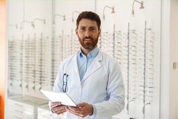ophthalmologist with eyeglasses using digital tablet while working in optics store