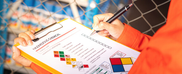 Extreme close-up at industrial worker'hand during verify on chemical and hazard material checklist, with background of chemical storage place. Industrial working with safety practice scene.
