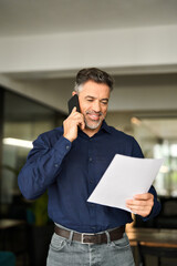 Happy busy mature business man holding documents making call at work. Smiling mid aged senior...