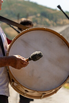 Detail of an elderly man's hand playing a large Galician folk drum or bass drum with a felt drumstick at a popular festival in a Galician town on a sunny day.