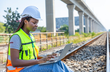 Fototapeta premium young african female engineer working on laptop to check railway tracks for maintenance at railroad,concept of safety quality control,rail transport,transportation industry