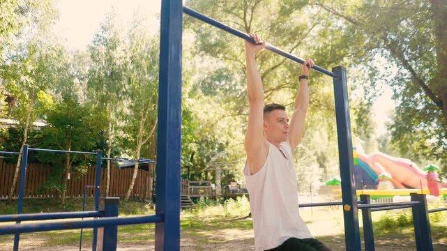 Handsome pumped up young male bodybuilder doing exercises on horizontal bar and parallel bars outdoors on the street. Beautiful male body shapes, beauty and health, training and motivation