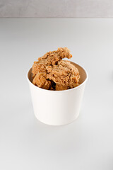 A stack of crispy fried chicken in a white bucket.
