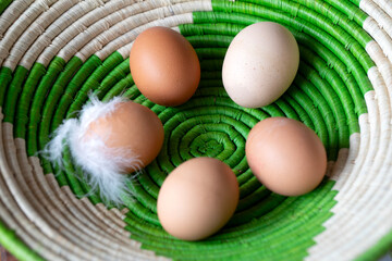 NATURAL WOVEN COLOURFUL BASKET OF ORGANIC BROWN CHICKEN EGGS WHITE FEATHERS REMAIN ON ONE EGG