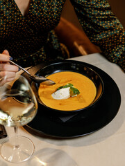 cute girl in a beautiful dress is eating a delicious cream soup with cream cheese, fresh vegetables, and fragrant herbs, served on a white plate in a cozy, charming restaurant