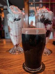 A closeup of a pint of Stout with two Ice Cream Sundae's in the background