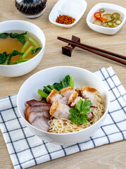 Red pork and crispy pork noodles on a wooden table
