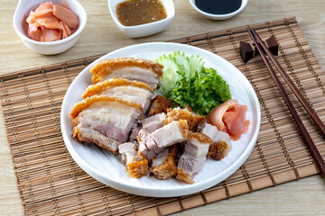 Crispy pork belly in a white plate on a wooden table