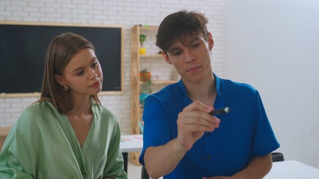 Two students, a female and a male, draw on a glass screen using a digital pen.