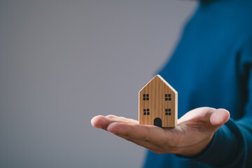 Hand holding miniature wooden house. Concept of real estate, home ownership, and housing market. Focus on the house against a neutral background.