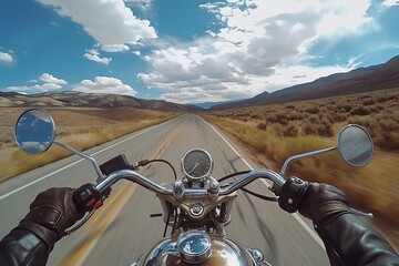 A motorcycle view on an open road surrounded by mountains and clouds.