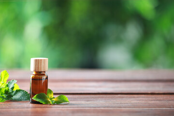 Bottle of mint essential oil and fresh leaves on wooden table, space for text