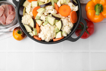 Cooking stew. Cut raw vegetables in pot and other ingredients on white tiled table, flat lay