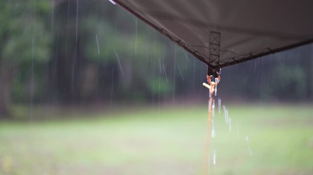 camping on rainy season with heavy rain water drips droplets to tip tarp and flow motion on fly sheet tent with carabiner paracord rope by holiday travel picnic on nature forest garden with rain sound