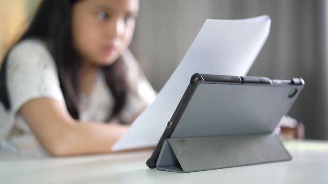 closeup computer tablet with blur asian child or kid girl reading on paper or study online class and learn from home by pad or young people studying learning by back to school technology education