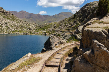 Abandoned wagon tracks on the side of a blue water pond with mountains in the background