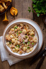 Pasta with chanterelles, bacon and cheese in plate on wooden table, top view, selective focus