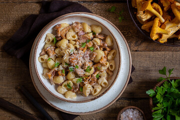 Pasta with chanterelles, bacon and cheese in plate on wooden table, top view, selective focus