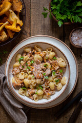 Pasta with chanterelles, bacon and cheese in plate on wooden table, top view, selective focus