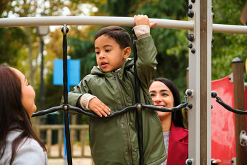 Obraz premium Latin lesbian couple playing with their son in the children's playground. LGBT family.