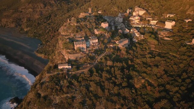 Aerial footage of the Tower of Nonza and the nearby coastal buildings at sunrise in Nonza, France