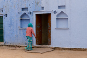 Rear view of unrecognized Indian woman entering in her house. Traditional Indian house facade with blue wall