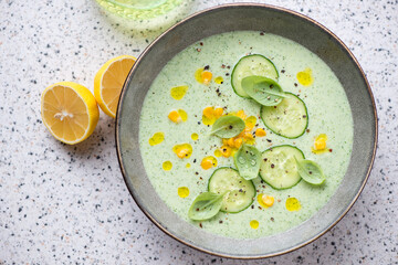 Plate with chilled cucumber and sweet corn soup, horizontal shot on a light-grey granite background, high angle view