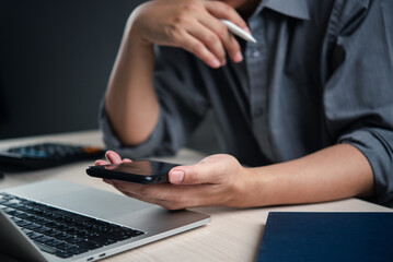 Person holding a smartphone while working on a laptop, symbolizing multitasking and modern business...