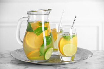 Freshly made lemonade with mint in jug and glasses on white marble table