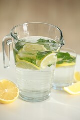Refreshing lemonade with mint in jug and glass on white table