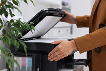 Woman using modern printer at workplace indoors, closeup