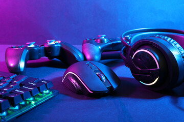 Computer mouse, headset, RGB keyboard and game controllers in neon lights on dark background, closeup © New Africa