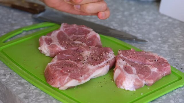 Woman peppering  raw pork slices on a green cutting board on a domestic kitchen. Close-up.