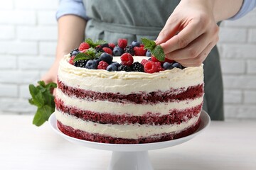 Woman decorating tasty sponge cake with mint at white table, closeup
