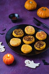 Halloween dessert, pumpkin cheesecakes with chocolate spider web decor on black ceramic plate on purple concrete background.