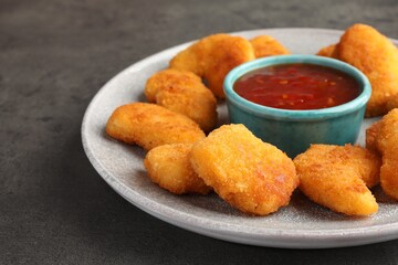 Plate with hot chili sauce and nuggets on grey textured table, closeup