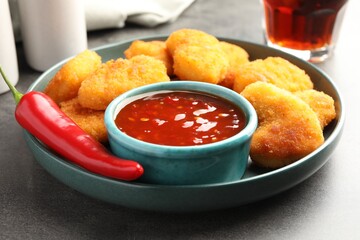 Plate with hot chili sauce, pepper and nuggets on grey textured table, closeup