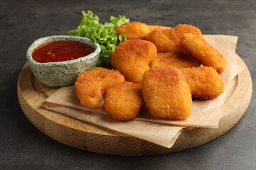 Board with hot chili sauce, lettuce and nuggets on grey textured table, closeup