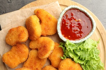 Board with hot chili sauce, lettuce and nuggets on grey textured table, top view