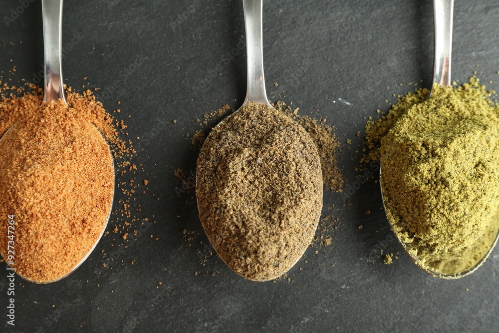 Sticker different superfood powders in spoons on black table, flat lay