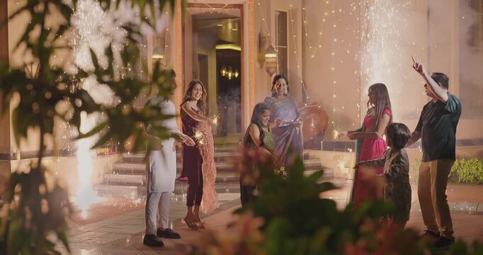 Indian Hindu Asian happy family teen girl boy child hold play crackers make fun joy night decor light diya home young adult male man female wife lady multi group older elder mom dad enjoy Diwali house