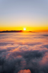 Golden sun rising behind mountains, illuminating a dreamy sea of clouds