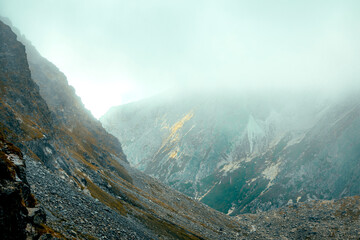Misty mountain landscape with steep rocky slopes and soft light breaking through the fog in the distance. Mengusovska Dolina © Iryna