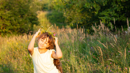 A beautiful girl adorned with a vibrant flower crown is playing in a sunlit, lush field