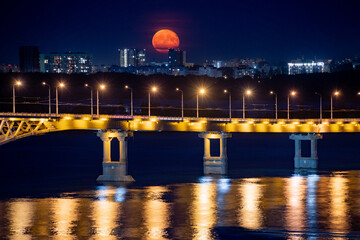 The full moon rises at night. The bridge over the Volga River between the cities of Saratov and Engels, Russia.