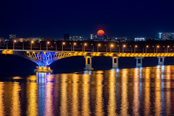 The full moon rises at night. The bridge over the Volga River between the cities of Saratov and Engels, Russia.