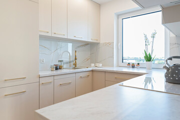 Fototapeta premium Modern kitchen interior with luxurious furniture, gold faucet with kitchen sink and marble tile on the wall. Design of indoors architecture.