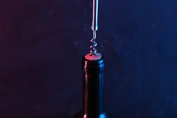 Wine bottle with corkscrew in lights on dark background, closeup